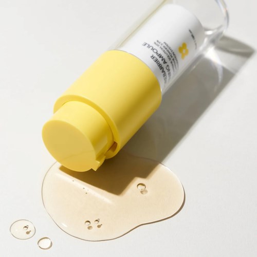 Een gele en witte lotionfles ligt op zijn zijde met lotion uitgesmeerd eromheen.