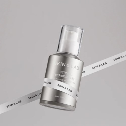 Een zilveren en witte fles huidherstellende serum met pomp, op een grijze achtergrond met een wit band met 'SKIN & LAB' opdruk.
