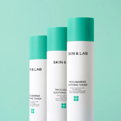 Drie witte flessen met turquoise deksels met het label 'Skin & Lab' tegen een licht turquoise achtergrond.