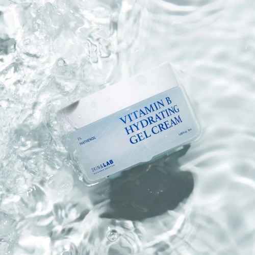 Een witte pot met label 'Vitamin B Hydrating Gel Cream' drijft in water met erond rimpels.