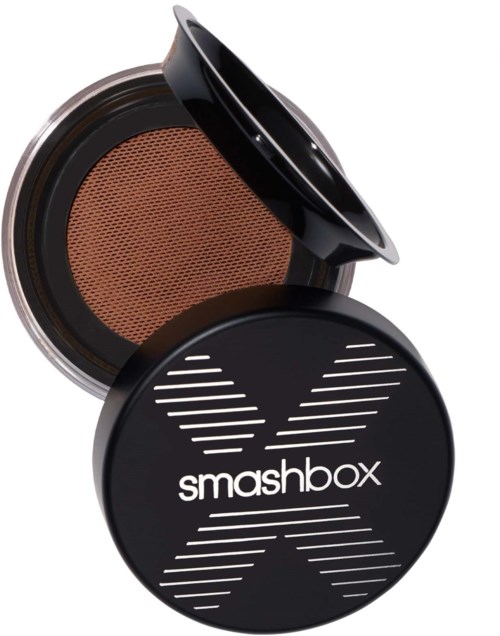 A black compact with powder inside and a lid showing the Smashbox logo. The powder has a brown tint.