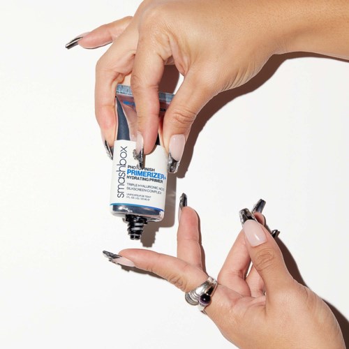 A hand applying a small blue and white tube of skincare product to fingertip. The background is white.
