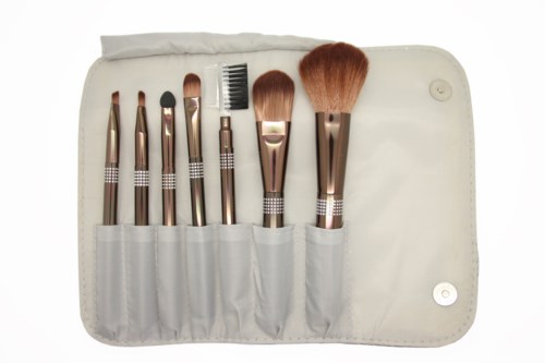 Makeup brushes in a white case with pockets, arranged from small to large, some with brown handles.