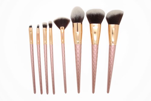 A set of eight makeup brushes with pink handles and gold ferrules, arranged from smallest to largest.