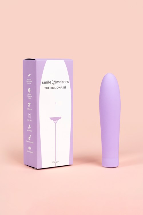 Ein lila Vibrator steht neben einer lila und weißen Schachtel mit Text, vor rosa Hintergrund.