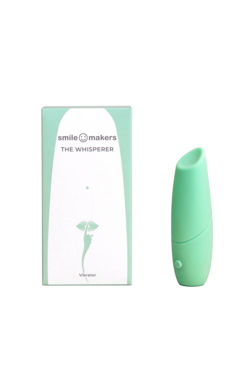 Ein kleiner, grüner, handgehaltener Vibrator neben seiner Schachtel mit der Aufschrift 'Smile Makers The Whisperer'.