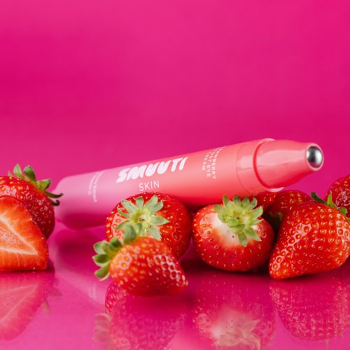 Aardbeien omringen een roze gezichtsroller op een roze achtergrond.