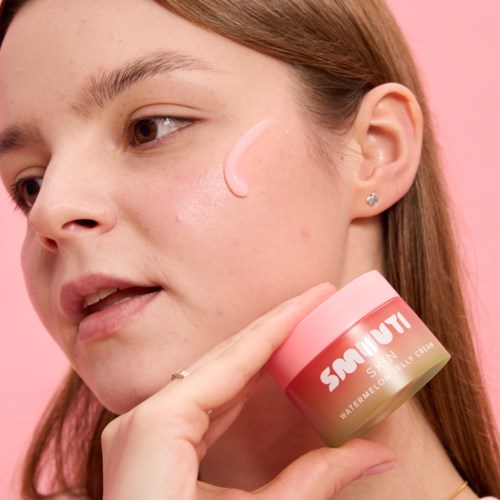Young woman applying pink skincare cream on her cheek, holding a jar labeled 'SOCOUNT Watermelon Jelly Cream.'