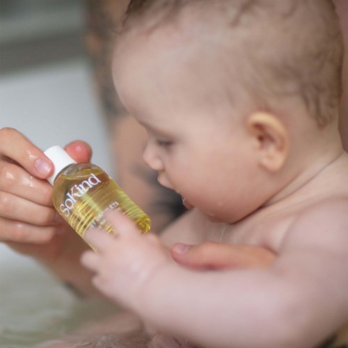 Ein Baby erhält Medizin oder Öl aus einer kleinen Flasche von einem Erwachsenen. Das Baby ist im Wasser oder Bad.