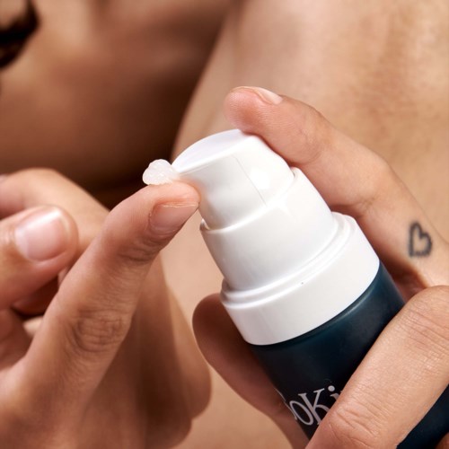 Jemand drückt auf eine weiße Pumpflasche, möglicherweise für Hautpflege oder Medizin, am Hand- oder Brustbereich.
