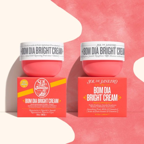 Zwei rosa Behälter von Bom Dia Bright Cream auf passenden rosa Schachteln mit weißen und gelben Etiketten vor einem verspielten pinken Hintergrund.