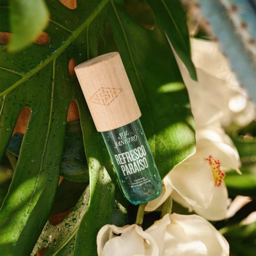 Ein Parfümflasche hängt zwischen grünen tropischen Blättern und weißen Blumen.