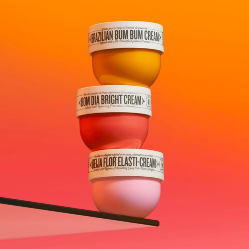 Tre färgglada krämburkar staplade, märkta: Brazilian Bum Bum Cream, Bum Dia Bright Cream, Abelha Flor Elasti-Cream.