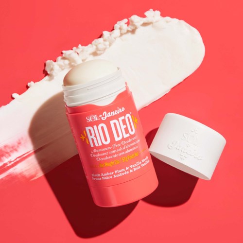 Fester Deodorantstift mit pinker Verpackung und weißem Deckel, auf rotem Hintergrund mit weißer Creme.