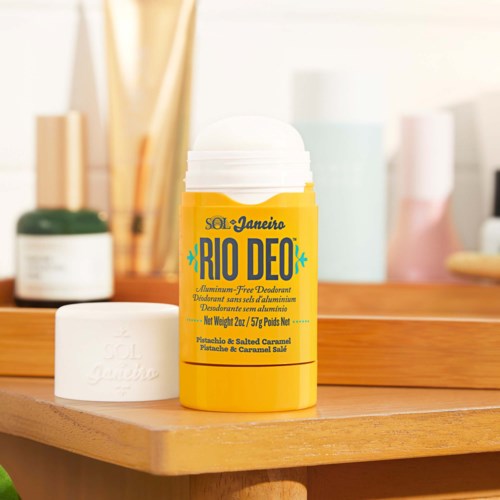 Ein gelbes und weißes Reisedöschen für Deo steht auf einer Holztischfläche, mit Badezimmer- oder Schminktisch im Hintergrund.