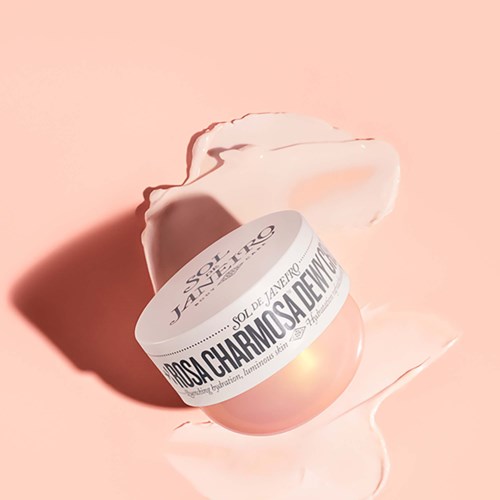 Ein pfirsichfarbes Schönheitsprodukt mit weißem Band auf Spanisch, umgeben von Creme oder Lotion auf rosa Hintergrund.