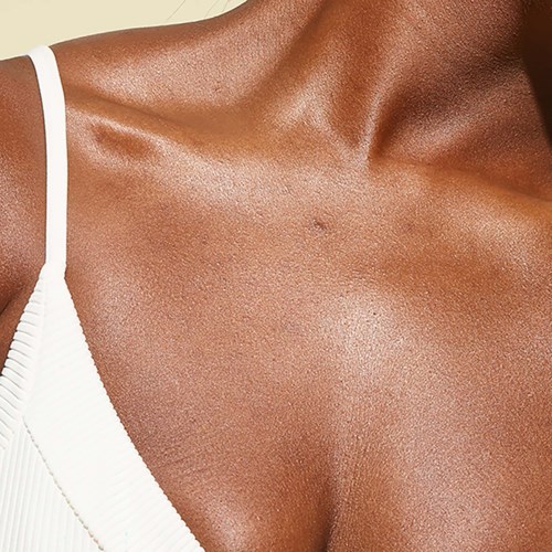  Nahaufnahme eines Schulters und oberen Brustbereichs einer Person, mit glatter, sonnengebräunter Haut und weißem Trägeroberteil.