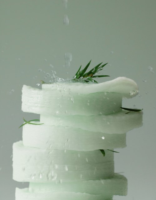 A block of white soap with green leaves, water drops, and a splash on a reflective surface.