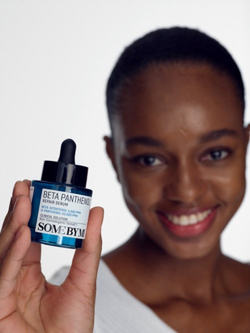 A smiling woman holds a blue dropper bottle labeled 'SOME BY' and 'BETA PANTHENOL REPAIR SERUM'.