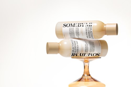 Two bottles are balanced on a clear glass, with one bottle upside down. The bottles have white labels with black text.