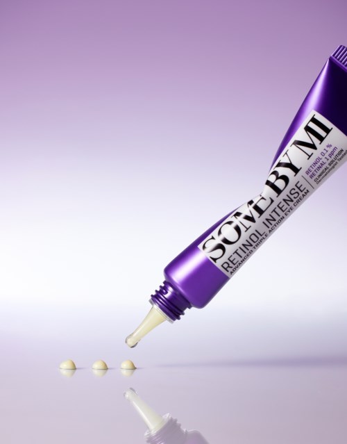 Een paarse tube met retinolcrème met wat crèmebolletjes ernaast. De achtergrond is lichtpaars.