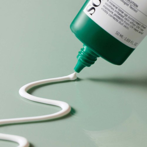 A green skincare tube squeezing out white cream on a light green surface.