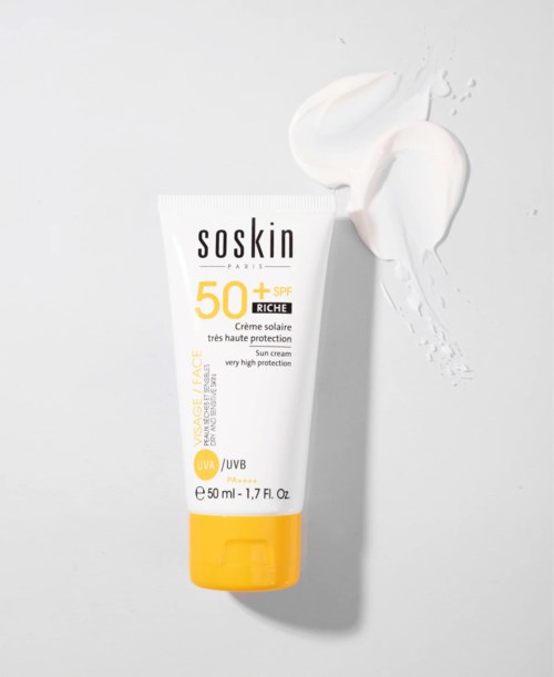 A white tube of sunscreen with a yellow cap and labeled SPF 50+ stands next to cream spill on light gray background.
