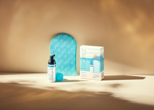 Ein blauer Tennisball und eine Packung St. Tropez Classic Sonnenschutzprodukt auf hellem braunem Hintergrund.