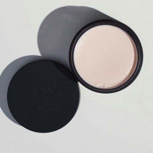 A round container with a black lid and pale pink cream inside.