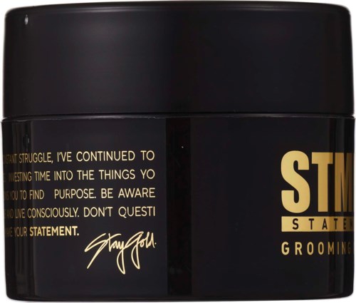 A black grooming product container with gold text and a signature message about purpose and self-awareness.