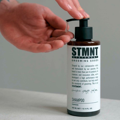 A person presses a pump on a brown bottle labeled 'STMT' shampoo.