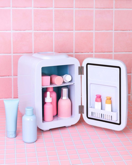Een klein roze kastje met flessen en containers voor schoonheids- of gezondheidsproducten, op een roze betegelde vloer.