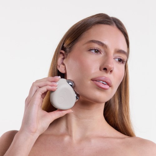 A woman uses a gadget on her neck, appearing to relax or enjoy a massage. She has long hair and a calm expression.