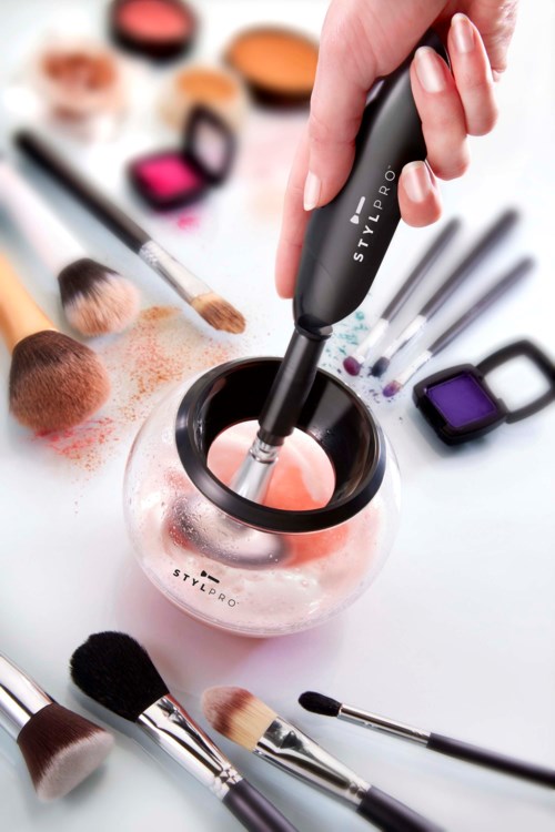Een hand gebruikt een gereedschap om make-up te mengen in een klein kommetje, omgeven door oogschaduw, blush en brushes.