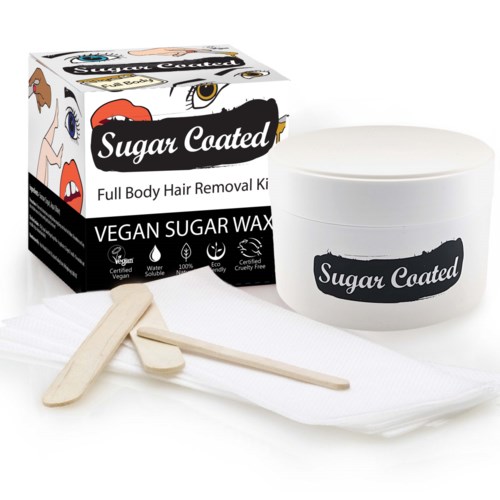 A box and container of vegan sugar wax for hair removal, with wooden spatulas and a cloth.