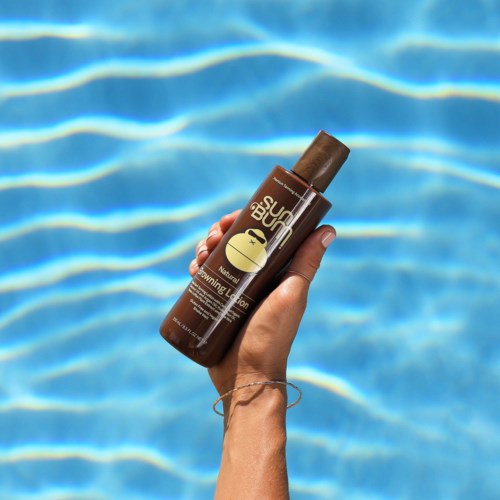 Eine Hand hält eine braune Sonnencreme-Flasche beim Pool mit klarem blauen Wasser. Sonnenschein scheint.