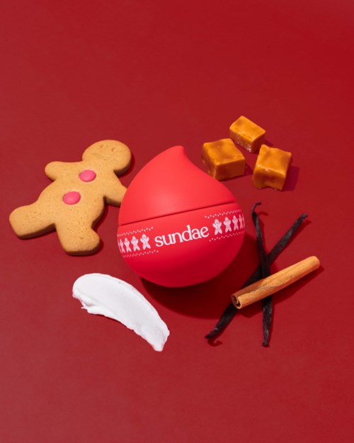 Rode doos met 'sundae' omgeven door koekjes, karamelstukjes, vanille en kaneelstokjes op een rode achtergrond.