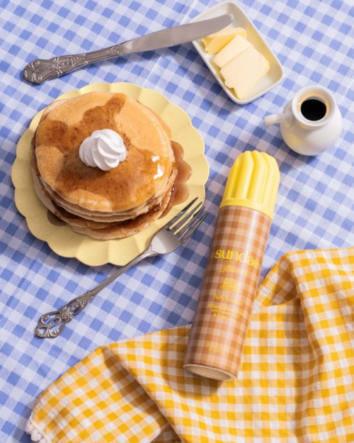 Stapel pannenkoeken met siroop, boter en slagroom op een blauwe ruitjeslap.