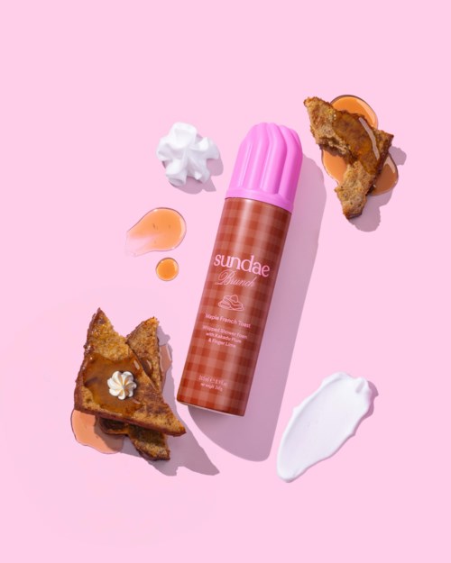 Een roze container met het label Sundae ligt tussen taartstukken, slagroom en saus op een roze achtergrond.