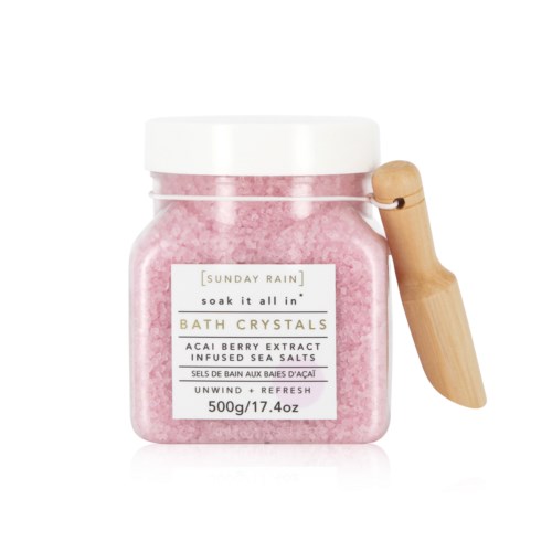 Roze badkristallen in een doorzichtige pot met houten lepel, label 'Sunday Rain'.
