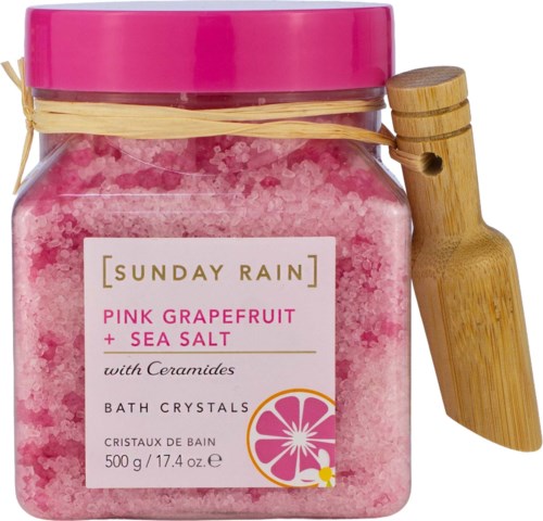 Rosa bade salt i en krukke med rosa lokk, merket Sunday Rain Pink Grapefruit og Sea Salt med Ceramides, med en tresleiv.