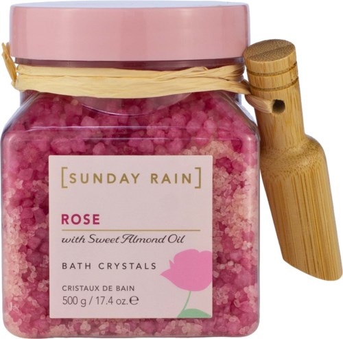 Lilla rosenbadkristaller med etikett for Sunday Rain Rose med mandelolje og en trefjøl.