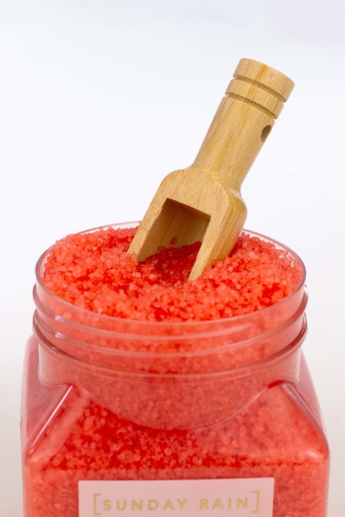 Orange badsalt i en klar burk med en träslev.