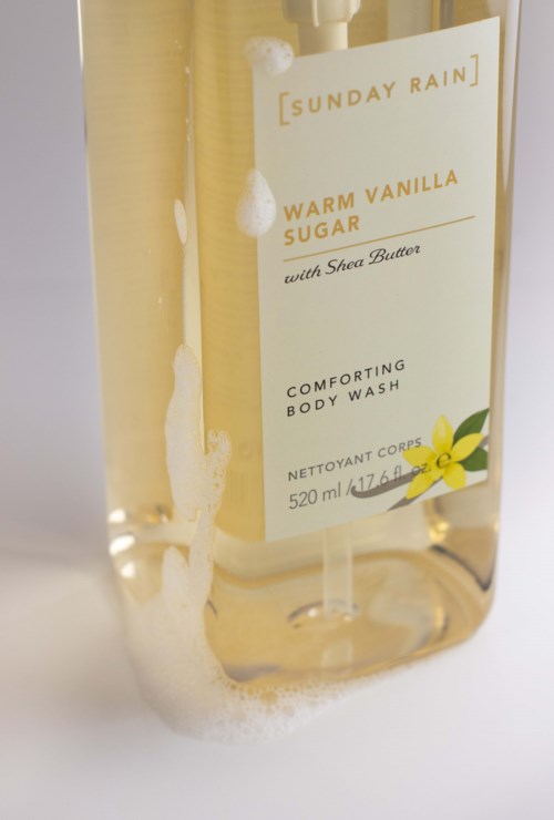 Läpinäkyvä vartalovaahtopullo, jossa on etiketti sanoo Warm Vanilla Sugar ja keltainen kukkakuva.