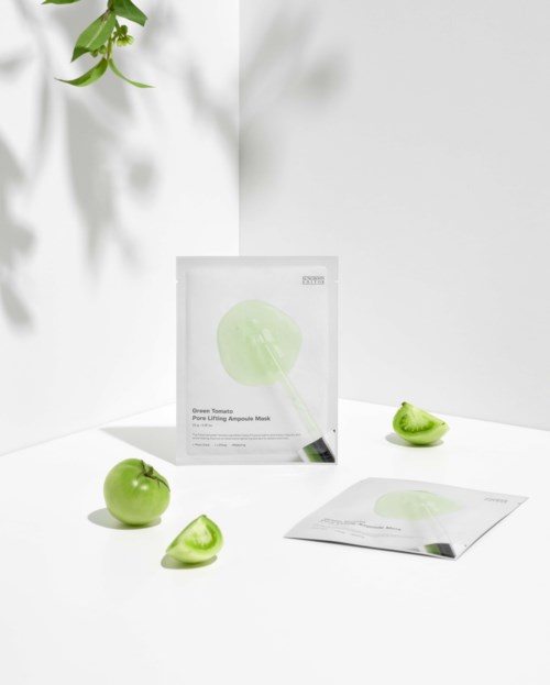 Een huidverzorgingsmaskerpakket met groene appels eromheen, een appel doormidden gesneden, op een witte oppervlakte.