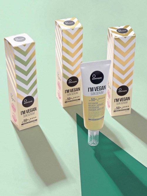 Drei Verpackungen und eine Tube veganes Sonnenschutzserum mit SPF 50 vor hellgrünem und teal Hintergrund.
