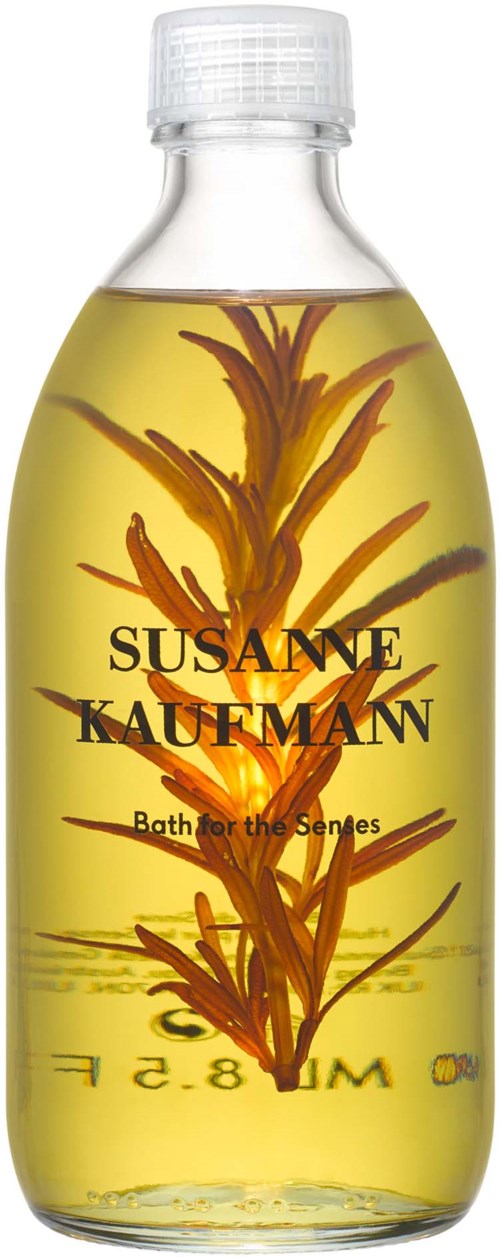 En tydlig flaska med gult vätska och växtliknande element inuti, märkt 'SUSANNE KAUFMAN Bath for the Senses'.