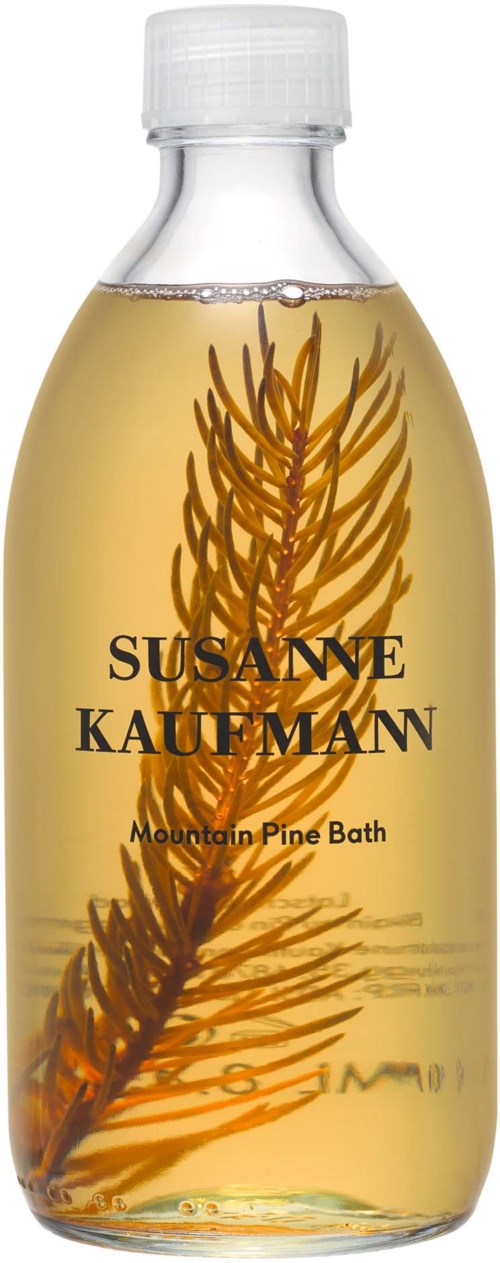 En tydlig flaska fylld med gult flytande innehåll och en tallgren inuti, märkt "Susanne Kaufman Mountain Pine Bath."