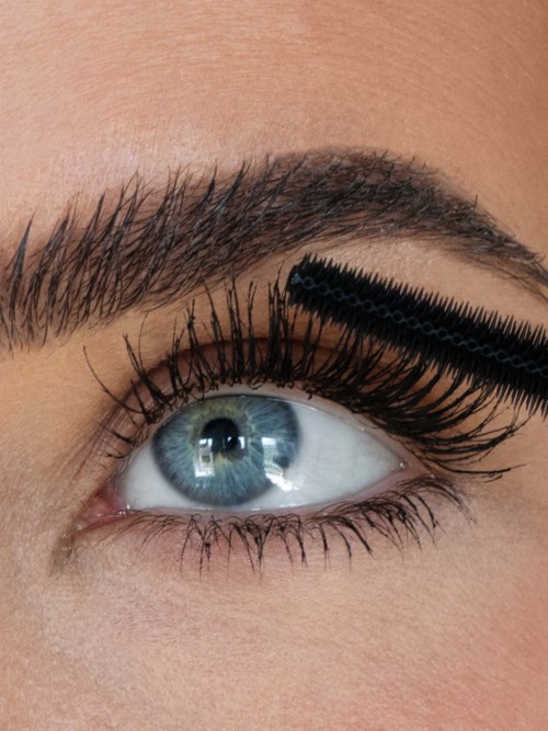 A close-up of an eye with makeup and a brush applying black mascara to the eyelashes.