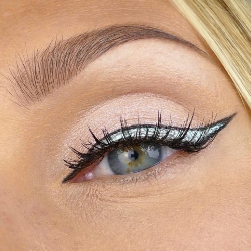 Närbild av ett mänskligt öga med tydlig make-up, långa ögonfransar och en skarp eyeliner. Blond hår nära.